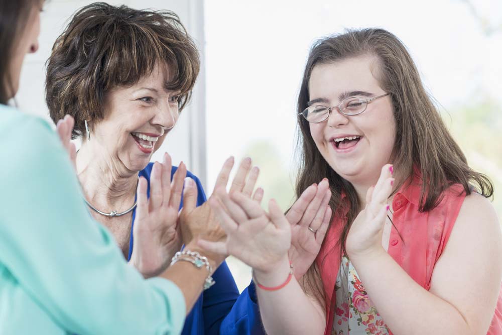 A happy teenage girl with down syndrome playing patty cake with her grandmother and mother.